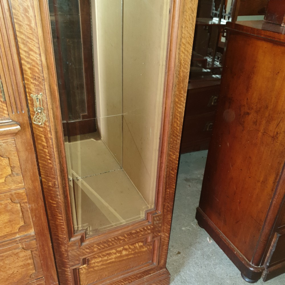 An Edwardian satinwood triple wardrobe featuring mirrored side doors, a central upper compartment, five drawers, and a stepped cornice top. View VIII