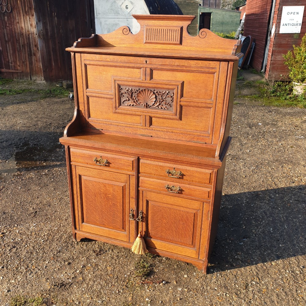 A late Victorian oak bureau cabinet featuring an open fall-front desk with an inset red leather writing surface, upper pigeonhole compartments, and lower double doors with brass handles. View II