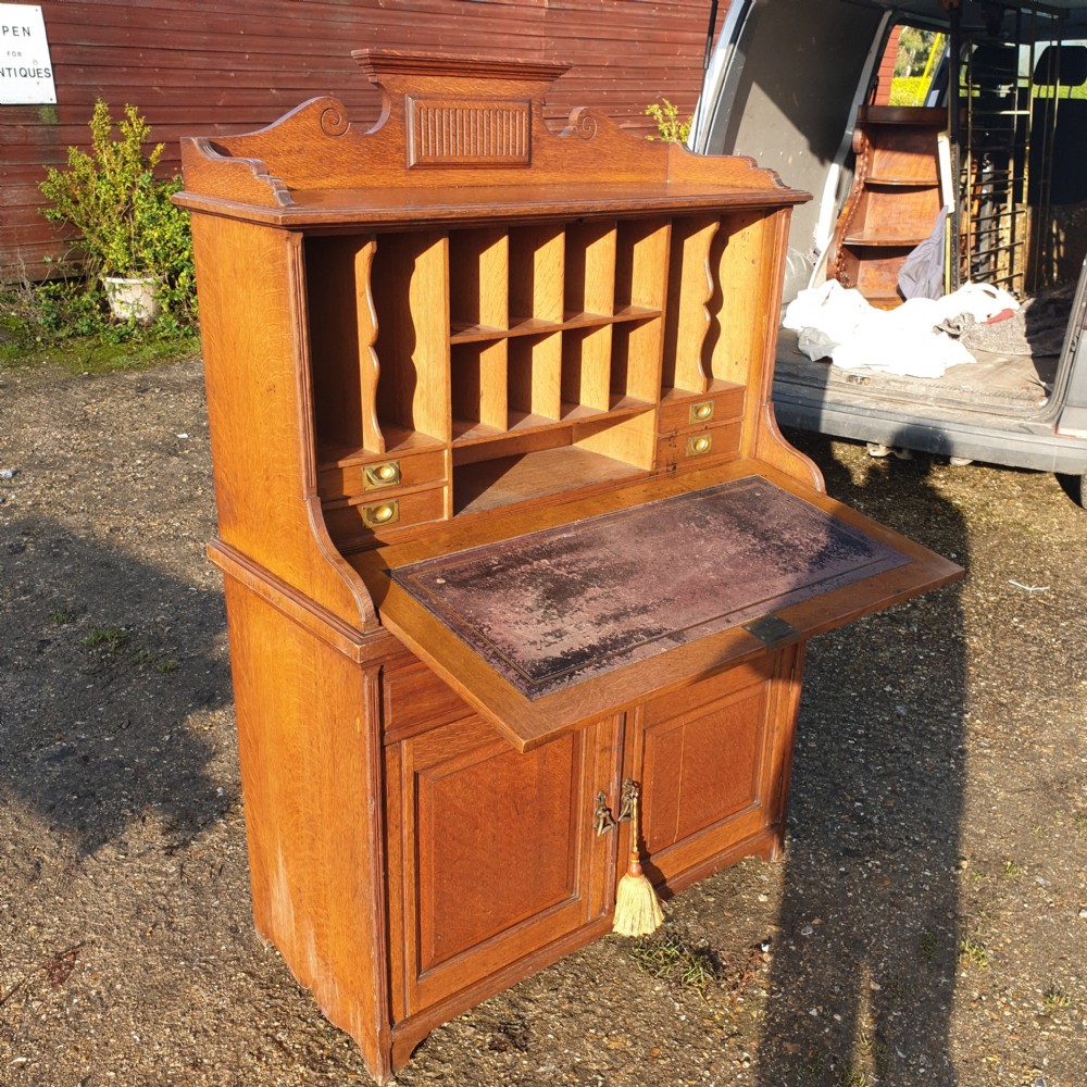 A late Victorian oak bureau cabinet featuring an open fall-front desk with an inset red leather writing surface, upper pigeonhole compartments, and lower double doors with brass handles. View III