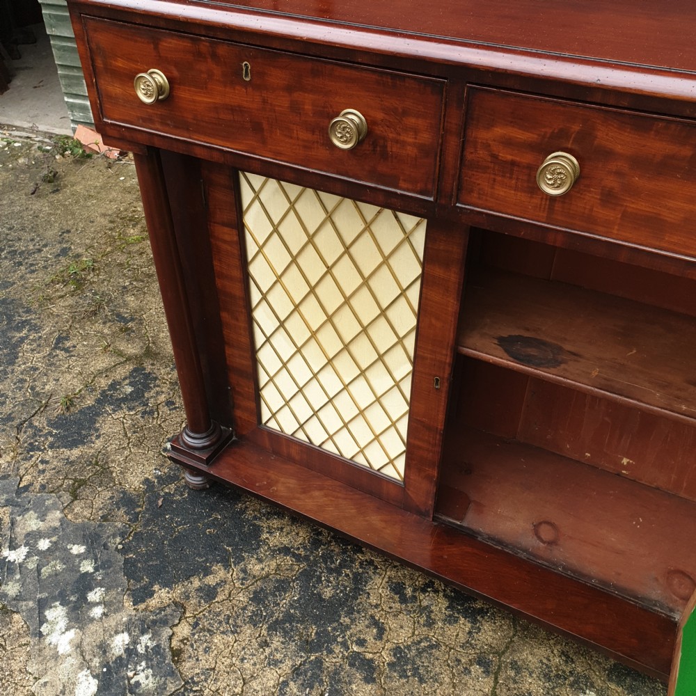 An antique Regency mahogany chiffonier cabinet featuring two raised shelves with turned supports, two drawers, and a double-door lower cabinet with brass lattice grilles and cream fabric backings. View II