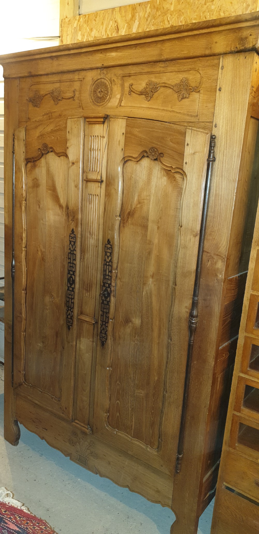 A tall French oak armoire featuring double panel doors decorated with carved floral motifs and long iron escutcheons.