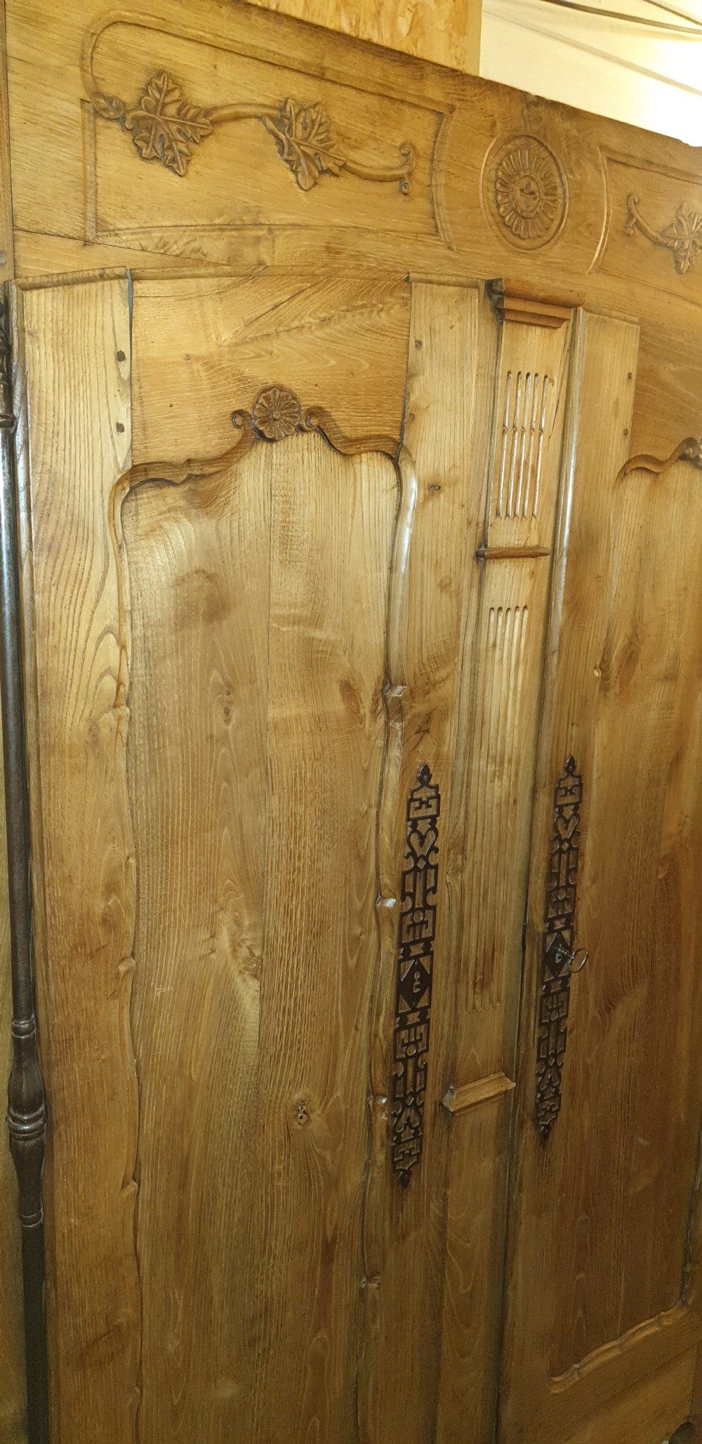 A tall French oak armoire featuring double panel doors decorated with carved floral motifs and long iron escutcheons. View VI