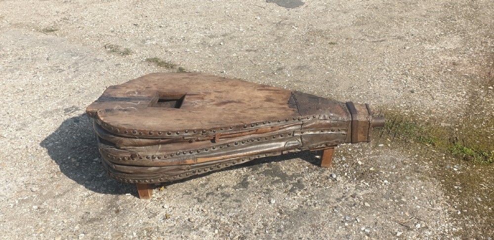 An antique blacksmith bellows converted into a low coffee table with timber boards, riveted leather sides, and wooden feet.
