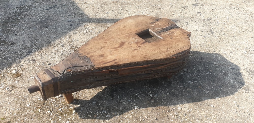 An antique blacksmith bellows converted into a low coffee table with timber boards, riveted leather sides, and wooden feet. View III