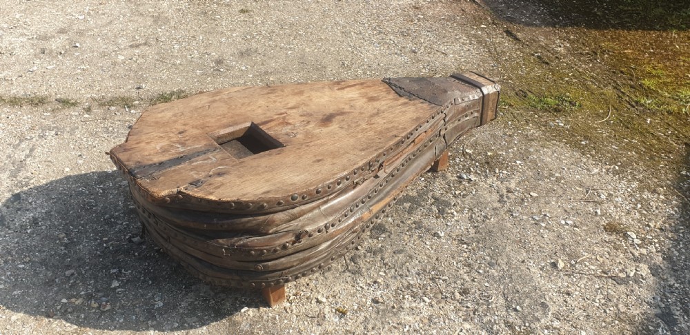 An antique blacksmith bellows converted into a low coffee table with timber boards, riveted leather sides, and wooden feet. View V