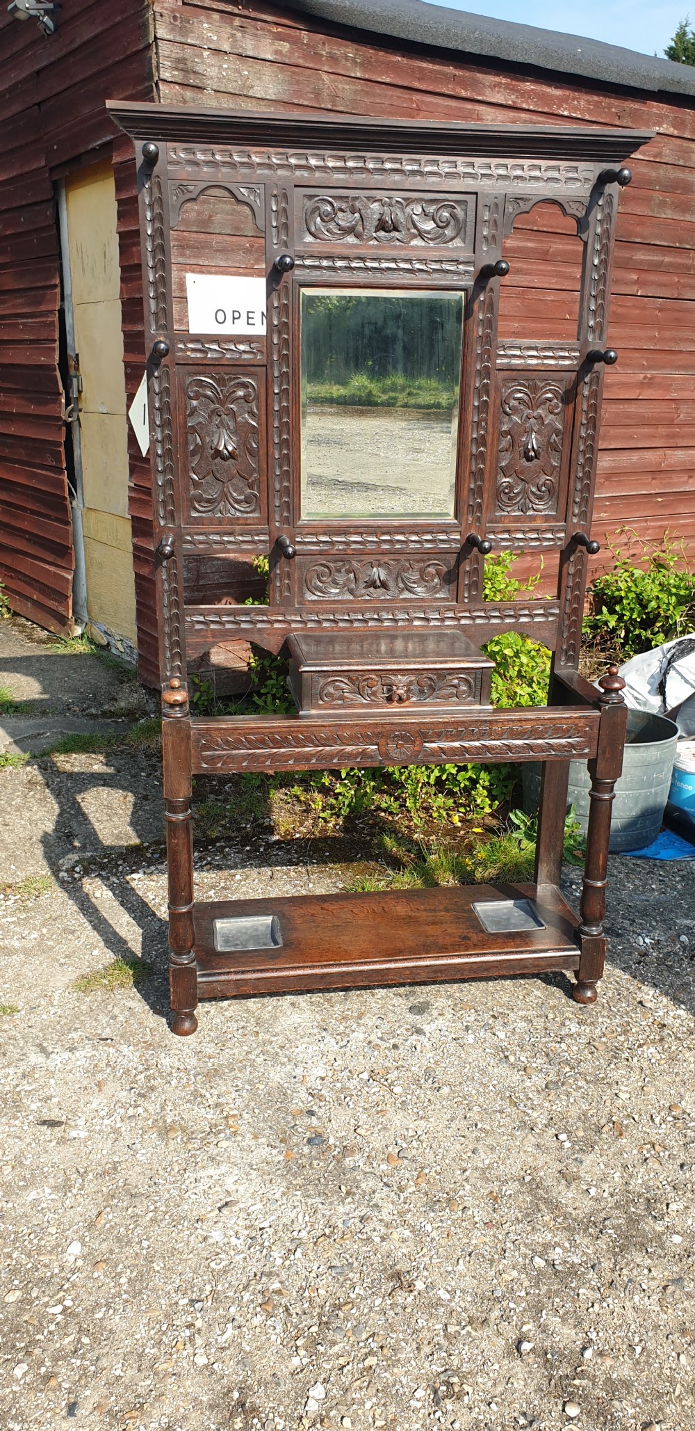 A late Victorian dark carved oak hallstand featuring a central mirror, carved Green Man motifs, coat pegs, a glove drawer, and integrated umbrella stands with metal drip trays.