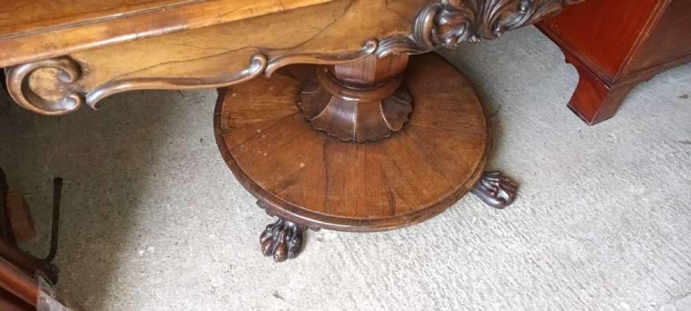 An early Victorian dark rosewood sofa table with a carved central apron motif, turned pedestal column, and circular platform base with scroll feet. View II