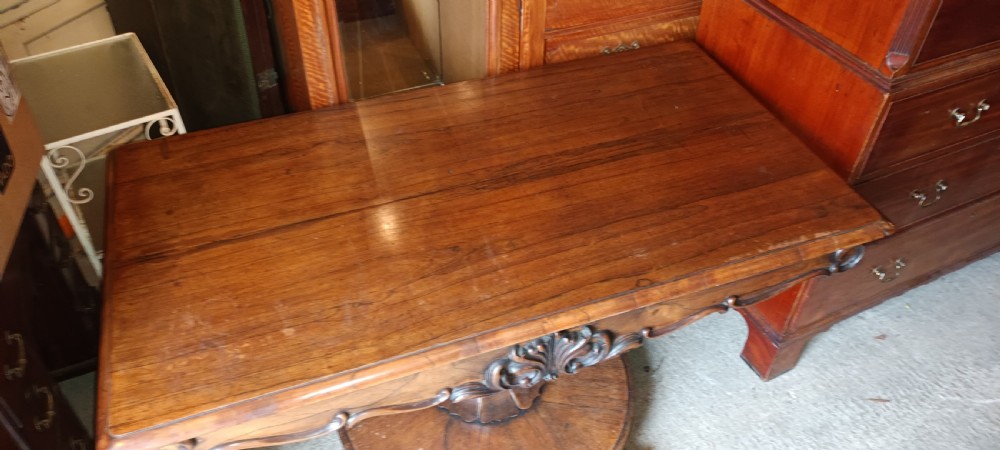 An early Victorian dark rosewood sofa table with a carved central apron motif, turned pedestal column, and circular platform base with scroll feet. View V
