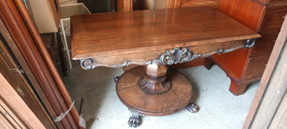 An early Victorian dark rosewood sofa table with a carved central apron motif, turned pedestal column, and circular platform base with scroll feet. View VIII