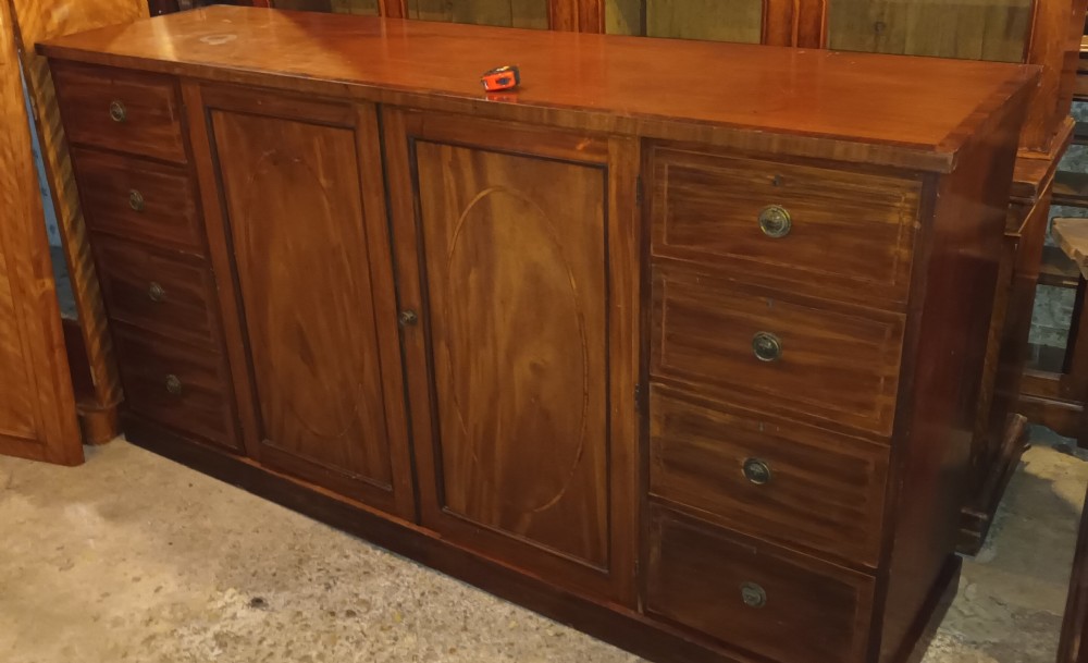 An antique warm brown mahogany dwarf linen press with central inlaid double doors flanked by two stacks of drawers and brass pull handles.