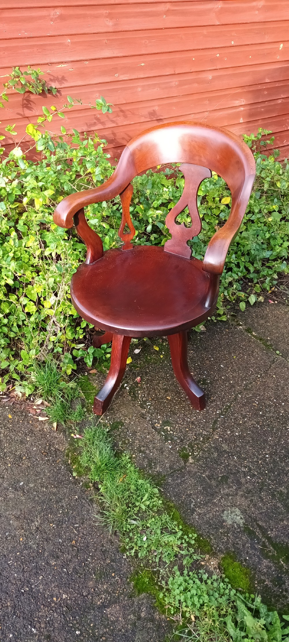 A late Victorian reddish-brown mahogany revolving desk armchair featuring a curved backrest with a pierced splat and a solid wooden seat resting on a swivel base.