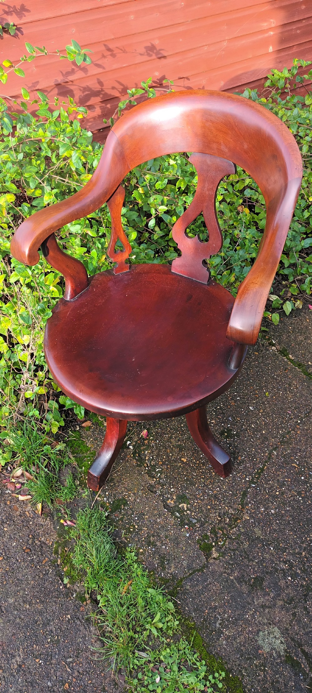 A late Victorian reddish-brown mahogany revolving desk armchair featuring a curved backrest with a pierced splat and a solid wooden seat resting on a swivel base. View II