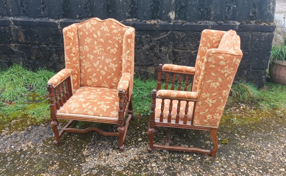 A pair of Edwardian high-back armchairs featuring carved oak frames, turned spindle arm supports, and patterned terracotta floral fabric upholstery.