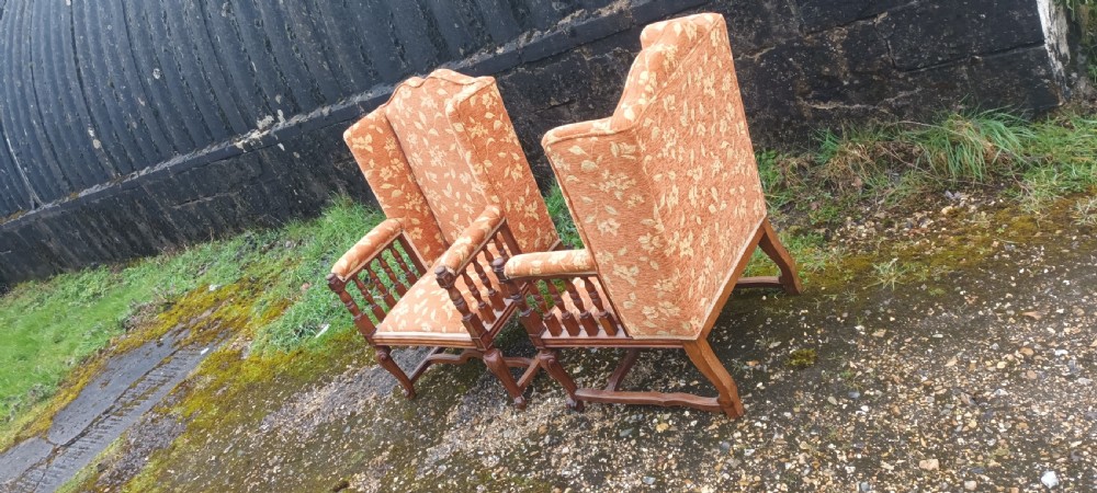 A pair of Edwardian high-back armchairs featuring carved oak frames, turned spindle arm supports, and patterned terracotta floral fabric upholstery. View II