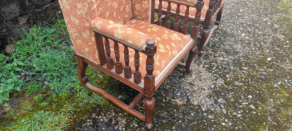 A pair of Edwardian high-back armchairs featuring carved oak frames, turned spindle arm supports, and patterned terracotta floral fabric upholstery. View III