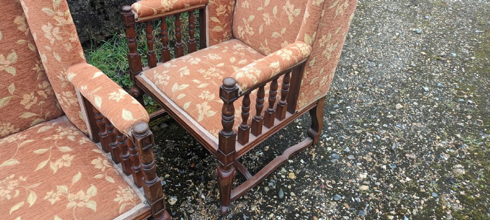 A pair of Edwardian high-back armchairs featuring carved oak frames, turned spindle arm supports, and patterned terracotta floral fabric upholstery. View IV