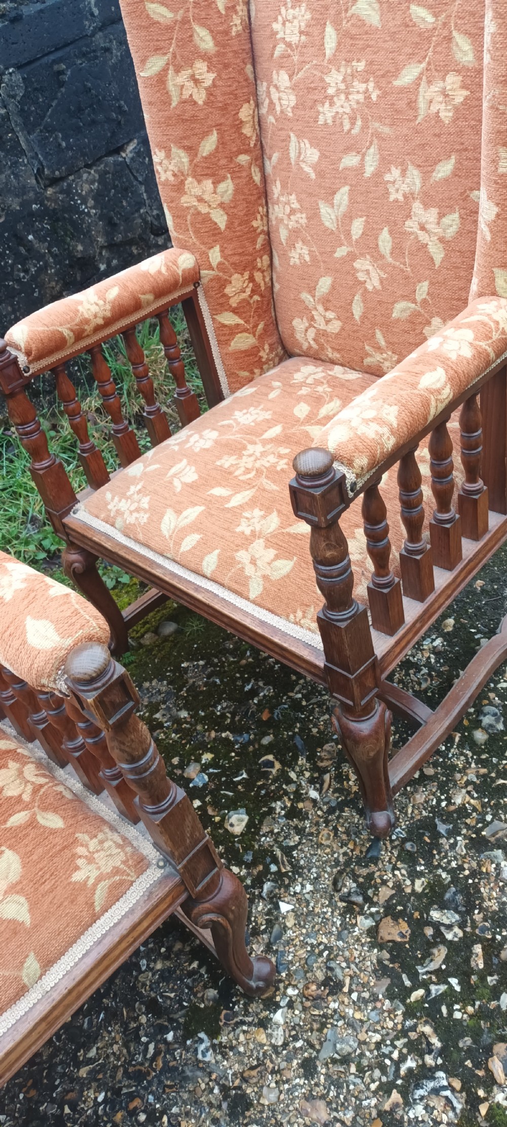 A pair of Edwardian high-back armchairs featuring carved oak frames, turned spindle arm supports, and patterned terracotta floral fabric upholstery. View VI
