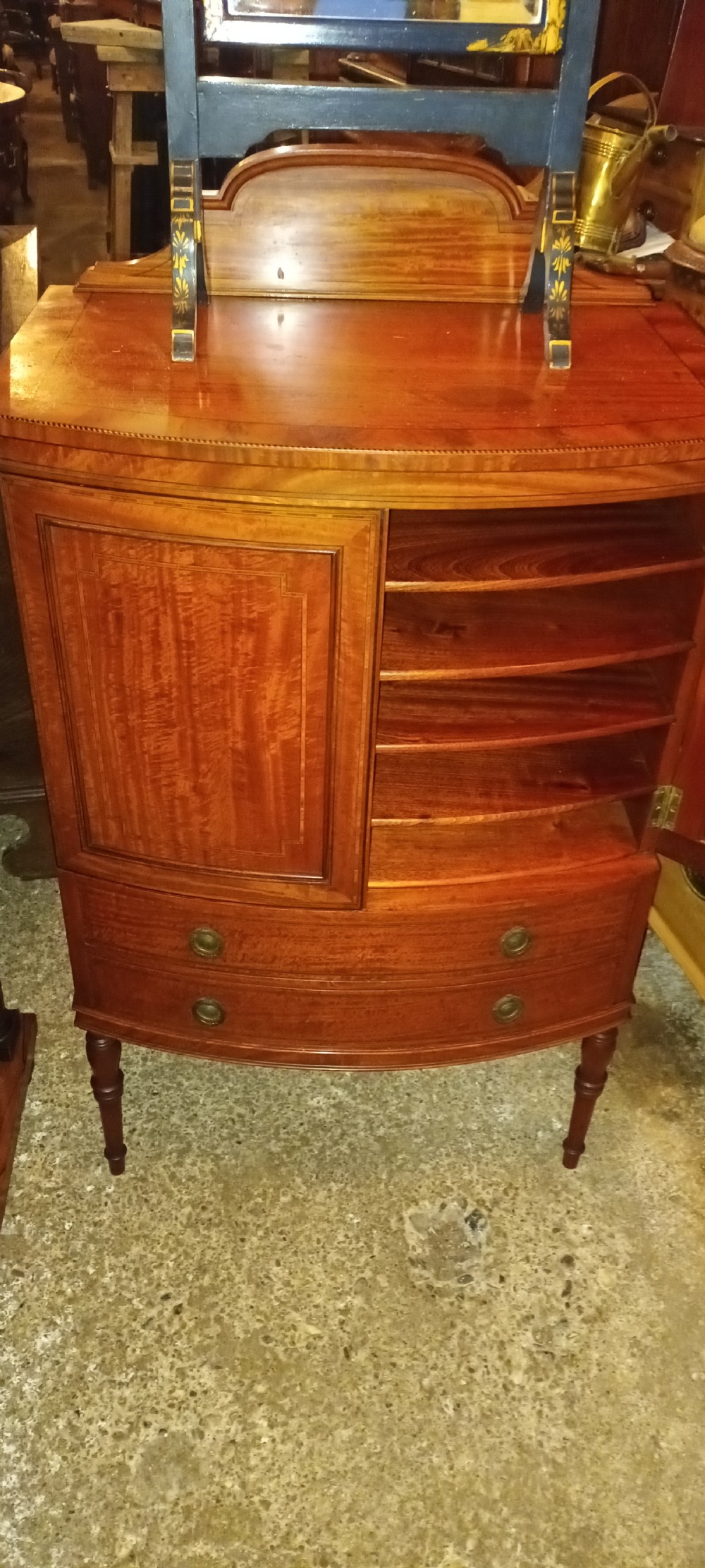 An Edwardian bowfront satinwood cabinet featuring inlaid door panels, two lower drawers, brass drop handles, and turned legs. View VIII