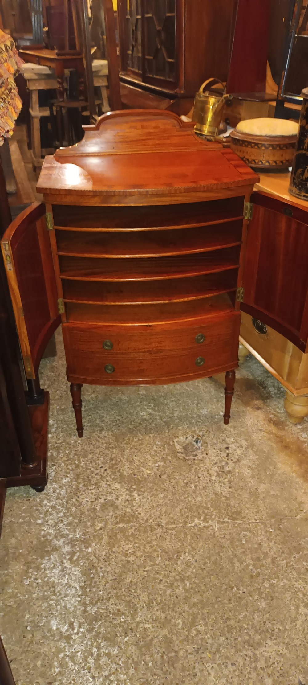 An Edwardian bowfront satinwood cabinet featuring inlaid door panels, two lower drawers, brass drop handles, and turned legs. View IX
