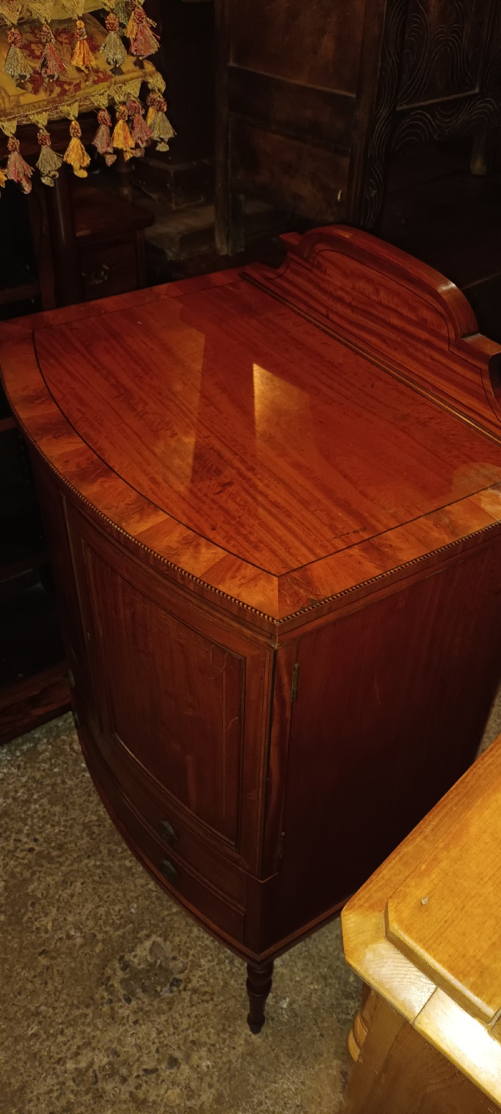 An Edwardian bowfront satinwood cabinet featuring inlaid door panels, two lower drawers, brass drop handles, and turned legs. View X