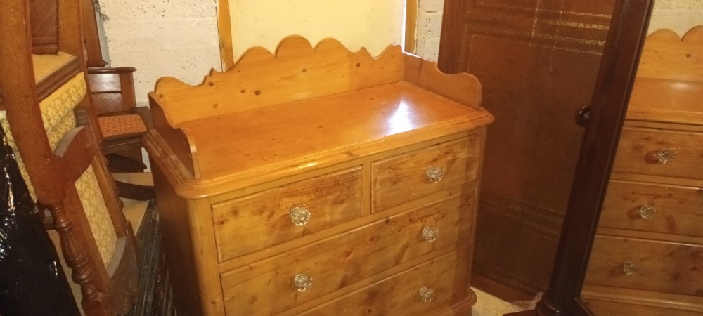 A Victorian pine chest of drawers featuring a scalloped gallery top, two short drawers over two long drawers, and clear glass knobs. View VI