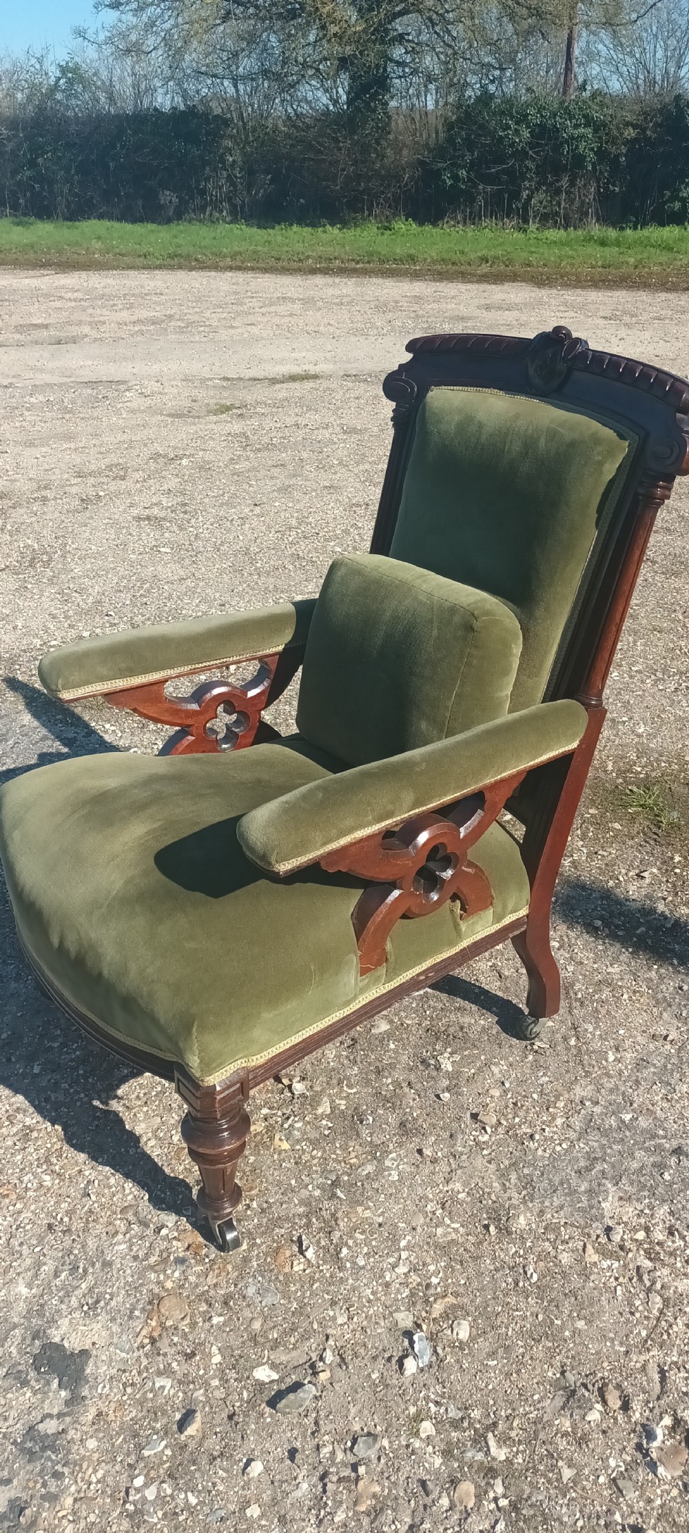 A late Victorian mahogany armchair upholstered in olive green velvet with carved openwork arm supports and turned front legs on castors. View III