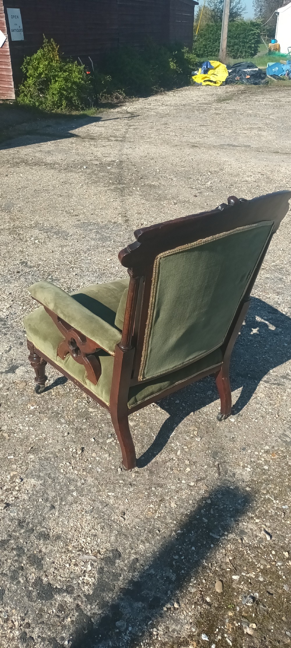 A late Victorian mahogany armchair upholstered in olive green velvet with carved openwork arm supports and turned front legs on castors. View IV