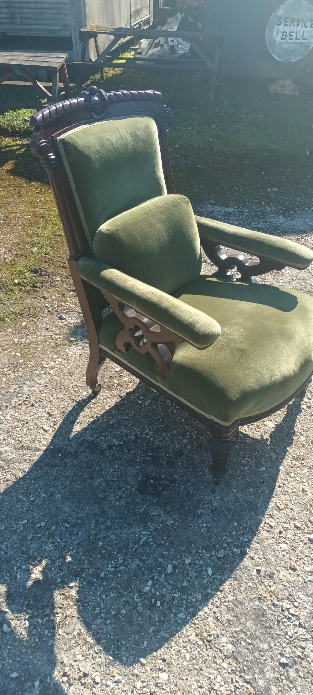 A late Victorian mahogany armchair upholstered in olive green velvet with carved openwork arm supports and turned front legs on castors. View V
