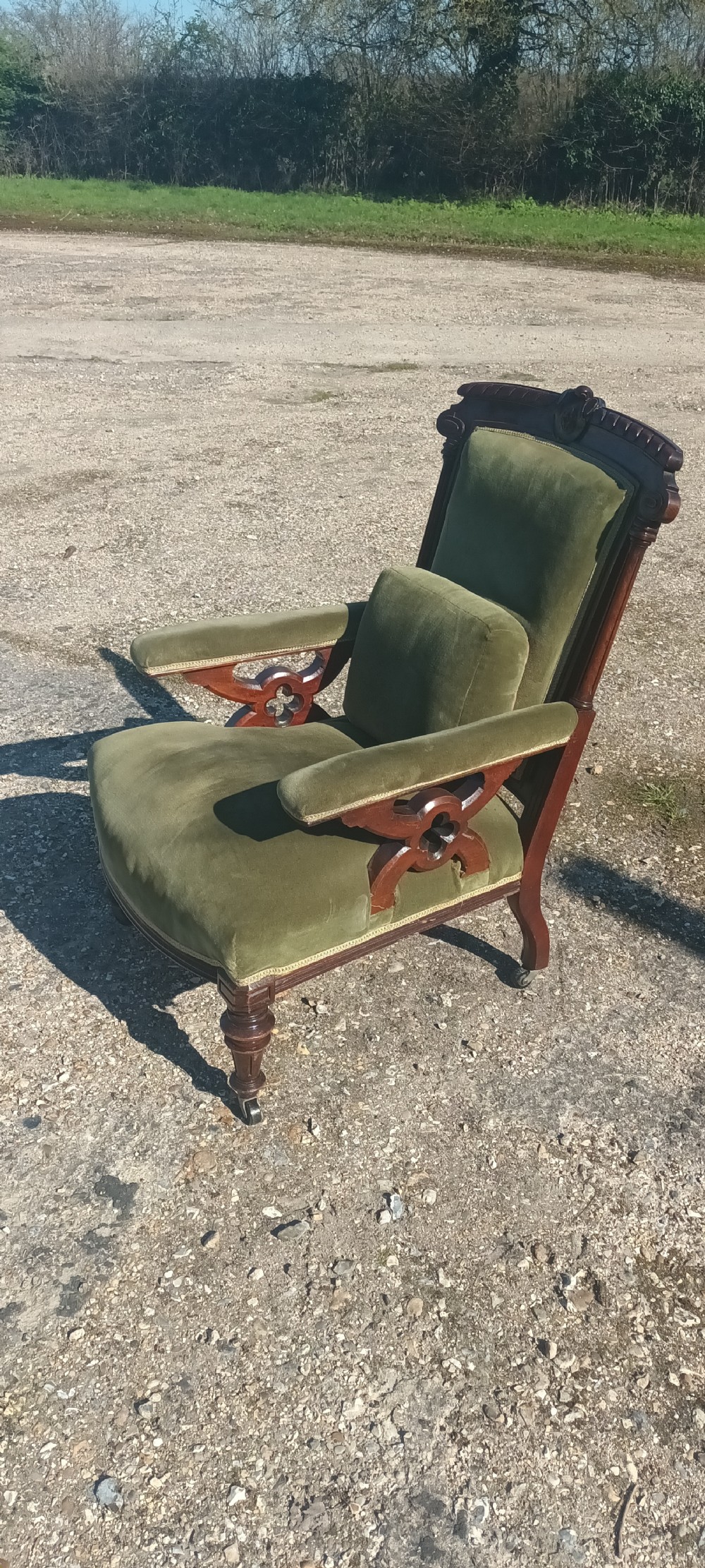 A late Victorian mahogany armchair upholstered in olive green velvet with carved openwork arm supports and turned front legs on castors. View VII