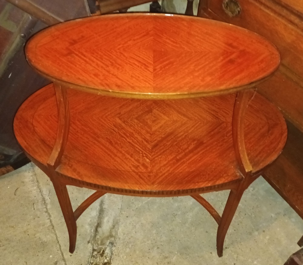An Edwardian oval two-tier satinwood etagere side table with diamond-matched wood veneer and swept legs.