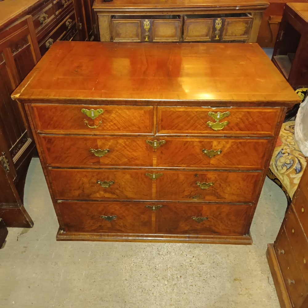 An early eighteenth-century figured walnut chest of drawers featuring two short over three long drawers with decorative brass plate handles. View II