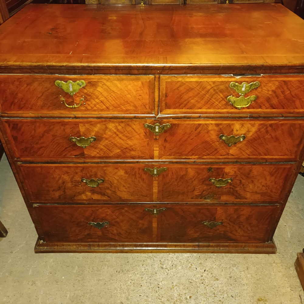 An early eighteenth-century figured walnut chest of drawers featuring two short over three long drawers with decorative brass plate handles. View V
