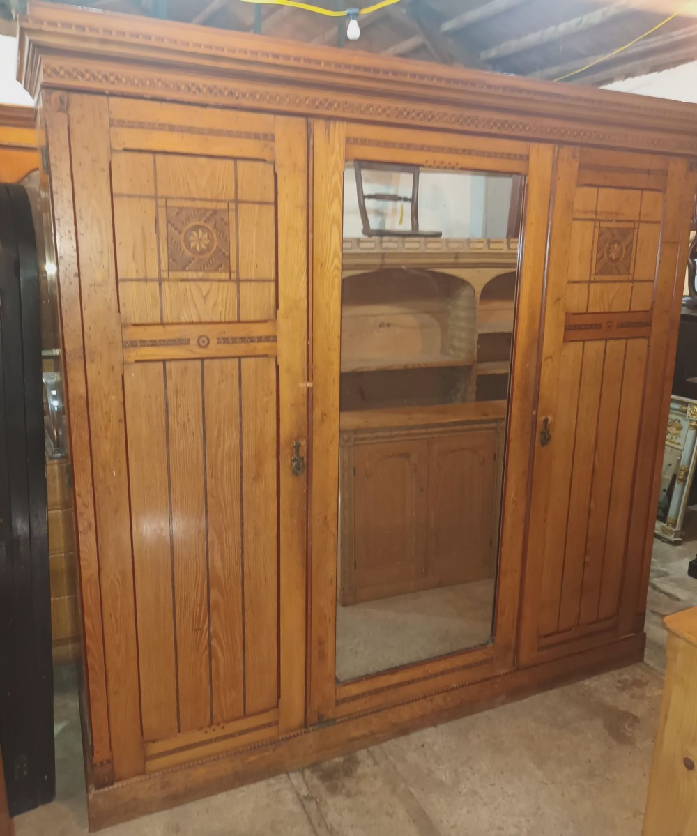 A large Victorian triple-door ash wardrobe featuring geometric marquetry inlay panels, a central mirrored door, and a heavily moulded upper cornice. View XXII