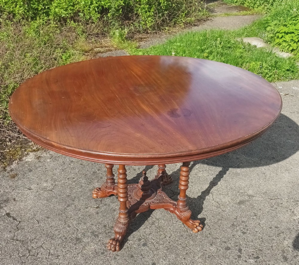 A late Victorian circular mahogany centre table featuring a polished top supported by turned columns and a carved base with carved feet.
