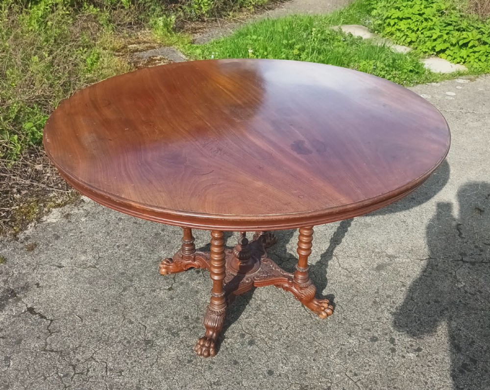 A late Victorian circular mahogany centre table featuring a polished top supported by turned columns and a carved base with carved feet. View IV