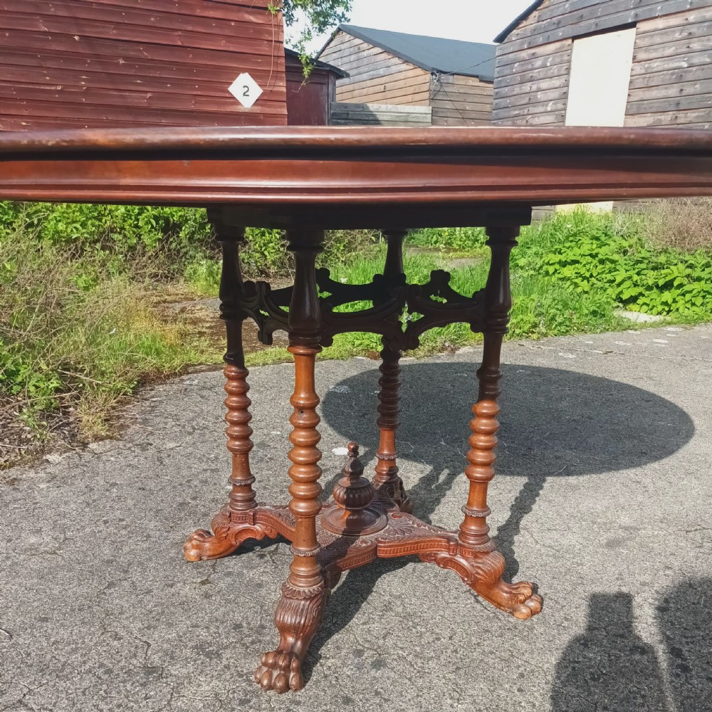 A late Victorian circular mahogany centre table featuring a polished top supported by turned columns and a carved base with carved feet. View V