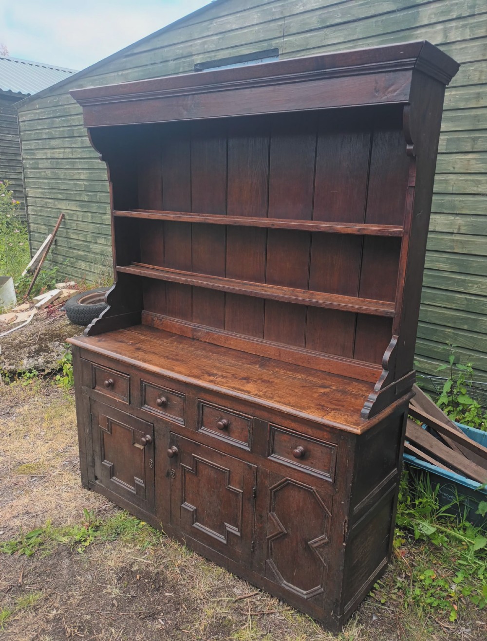 An antique two-part dark oak Welsh dresser featuring an upper plate rack with open shelves over a base cabinet with drawers and geometric panelled doors.