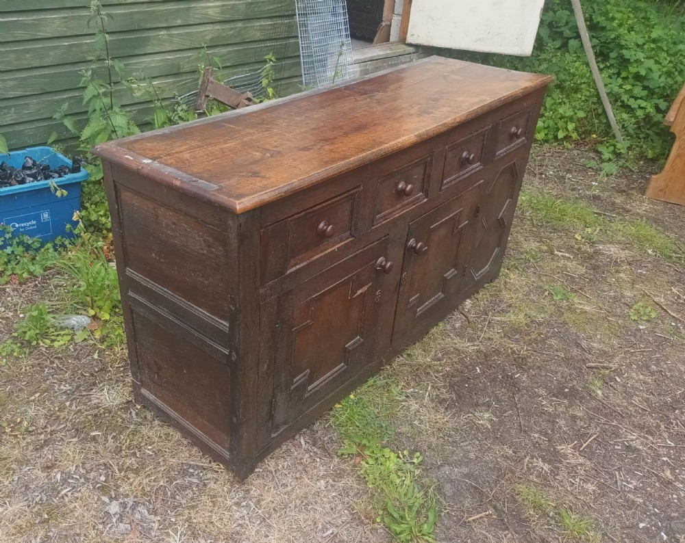 An antique two-part dark oak Welsh dresser featuring an upper plate rack with open shelves over a base cabinet with drawers and geometric panelled doors. View II