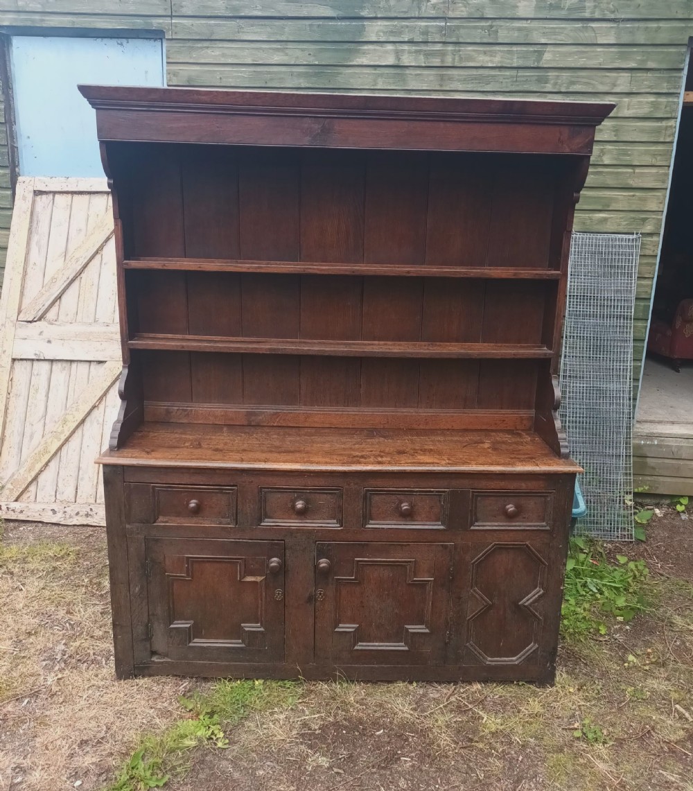 An antique two-part dark oak Welsh dresser featuring an upper plate rack with open shelves over a base cabinet with drawers and geometric panelled doors. View IV