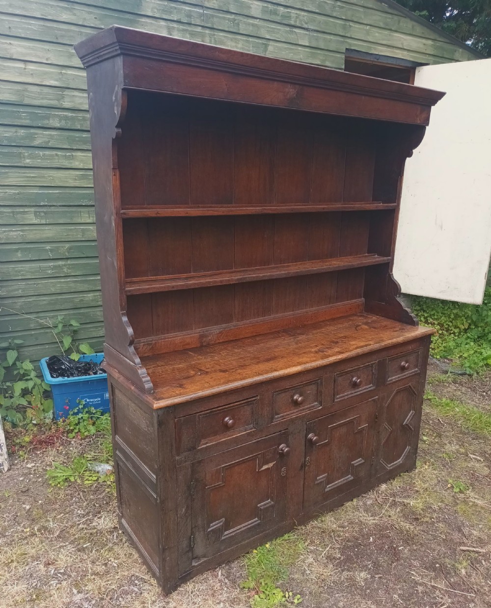 An antique two-part dark oak Welsh dresser featuring an upper plate rack with open shelves over a base cabinet with drawers and geometric panelled doors. View V