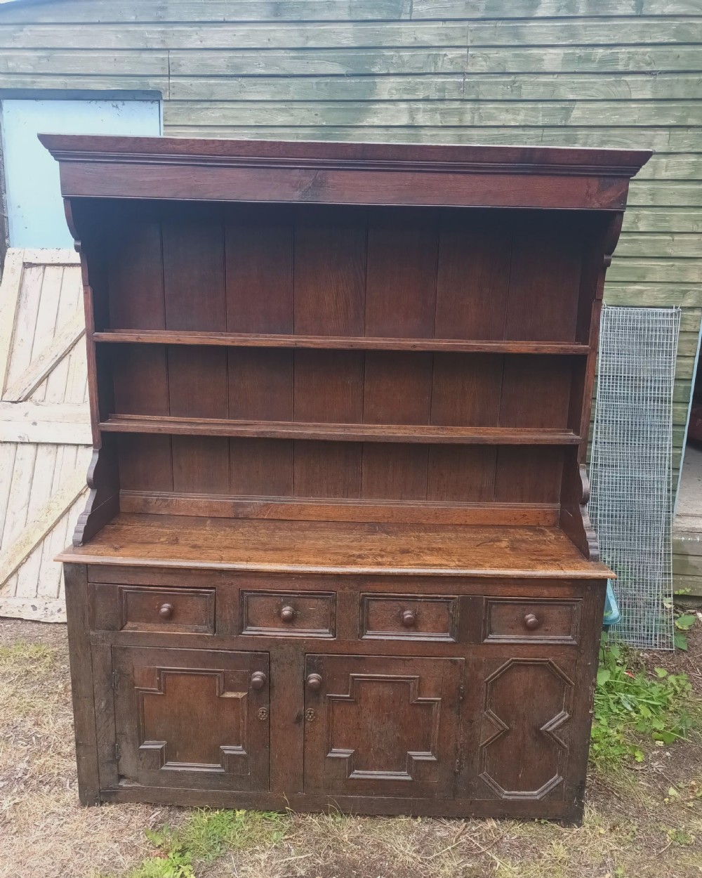 An antique two-part dark oak Welsh dresser featuring an upper plate rack with open shelves over a base cabinet with drawers and geometric panelled doors. View VII