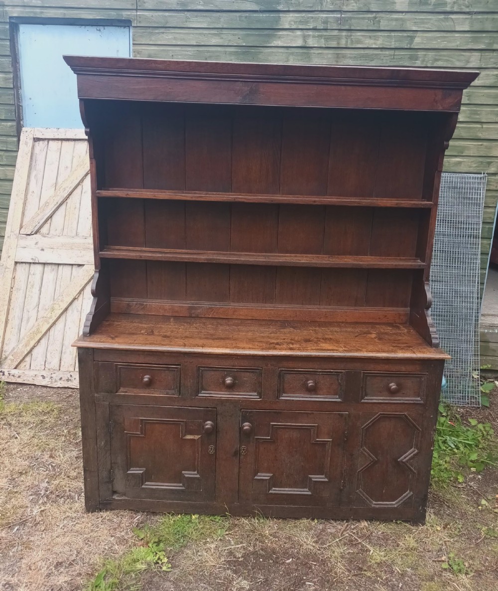 An antique two-part dark oak Welsh dresser featuring an upper plate rack with open shelves over a base cabinet with drawers and geometric panelled doors. View XII