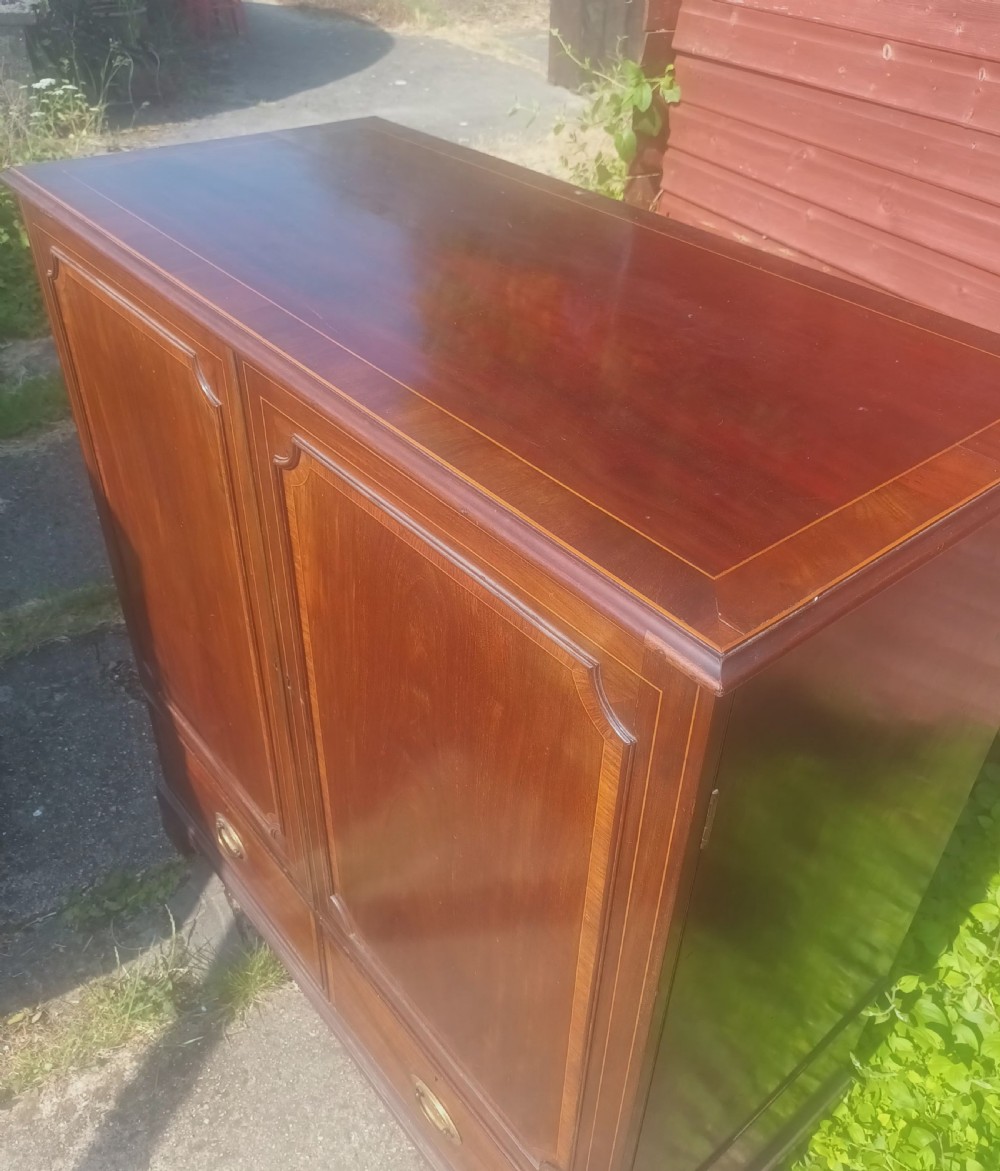 A warm brown mahogany dwarf linen press cupboard featuring two crossbanded cupboard doors above two lower drawers with brass handles. View IX