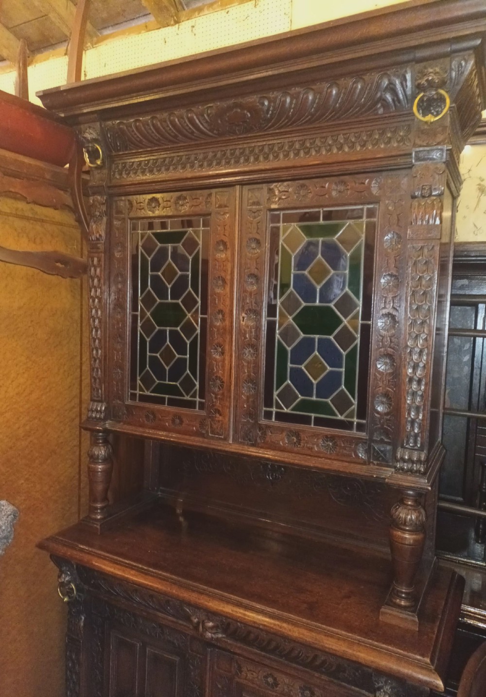 A dark Victorian carved oak bookcase with upper leaded glass doors, middle turned supports, and relief-carved lower panel doors. View V