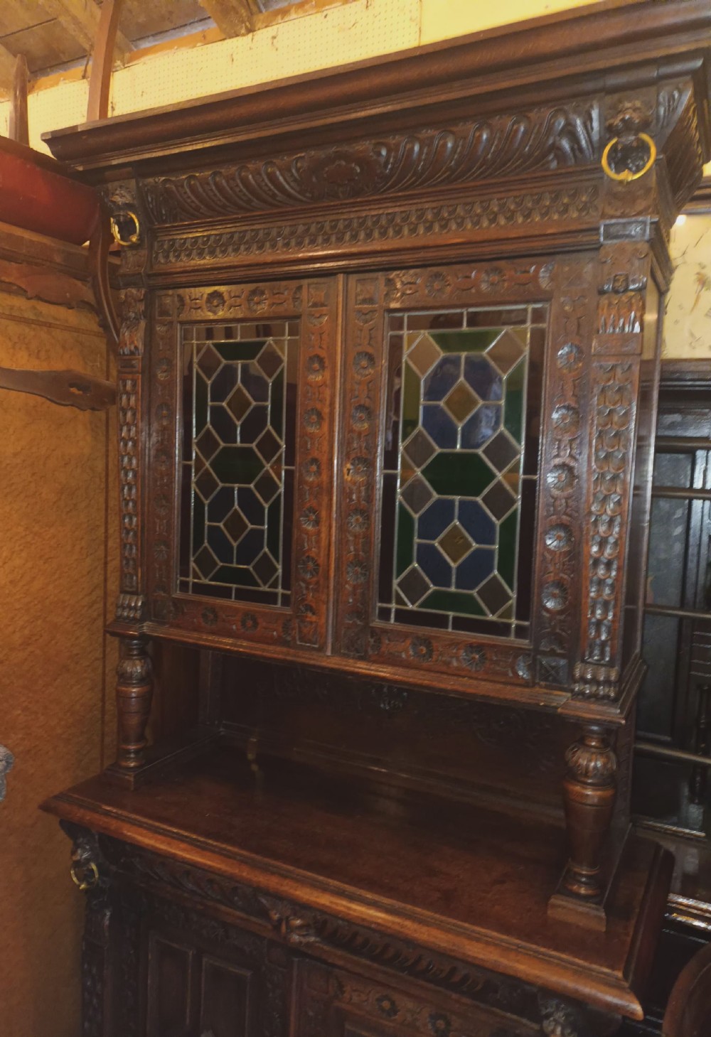 A dark Victorian carved oak bookcase with upper leaded glass doors, middle turned supports, and relief-carved lower panel doors. View VII