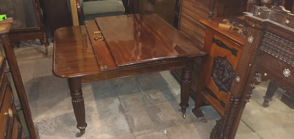 An extending Regency mahogany dining table with a polished flame veneer surface, three additional leaves, and reeded turned legs on brass castors. View XII