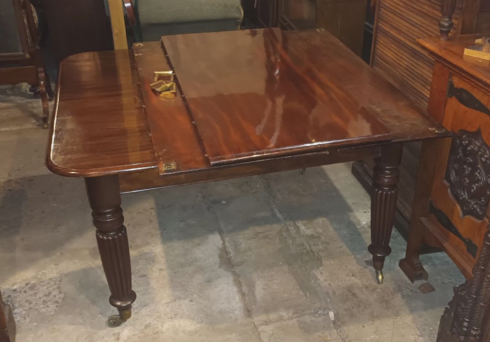 An extending Regency mahogany dining table with a polished flame veneer surface, three additional leaves, and reeded turned legs on brass castors. View XVII