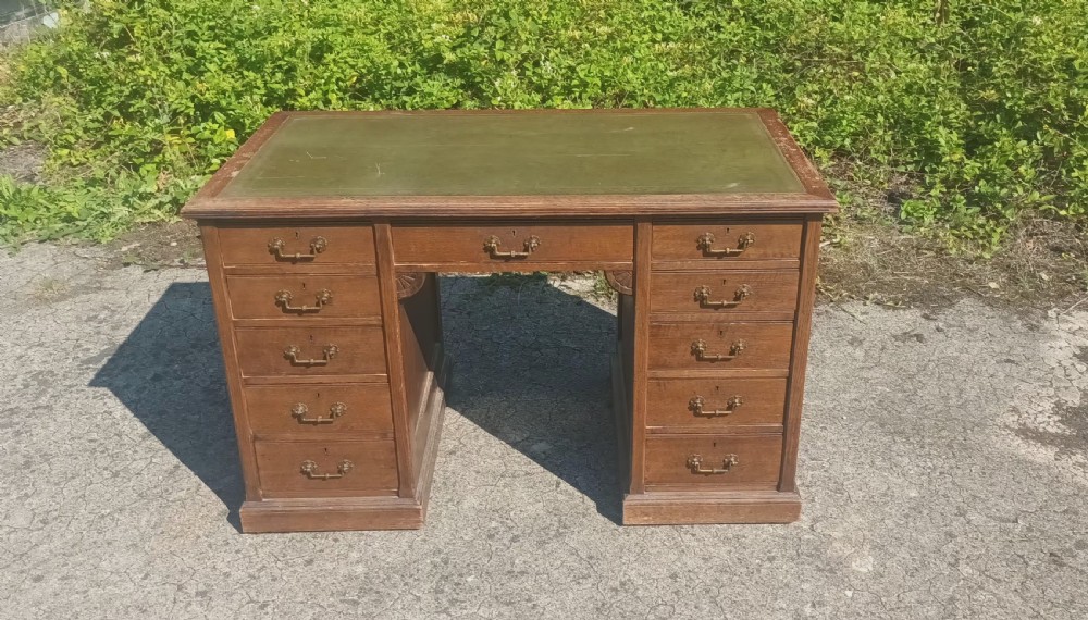 A late Victorian oak kneehole pedestal writing desk featuring nine drawers with brass handles and a green leather insert on the top surface.
