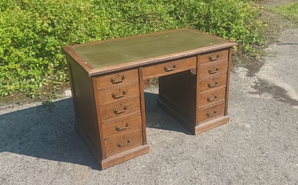 A late Victorian oak kneehole pedestal writing desk featuring nine drawers with brass handles and a green leather insert on the top surface. View VI