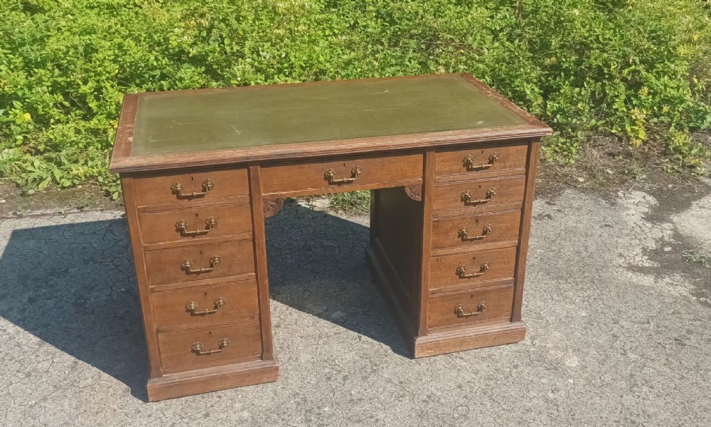 A late Victorian oak kneehole pedestal writing desk featuring nine drawers with brass handles and a green leather insert on the top surface. View VII